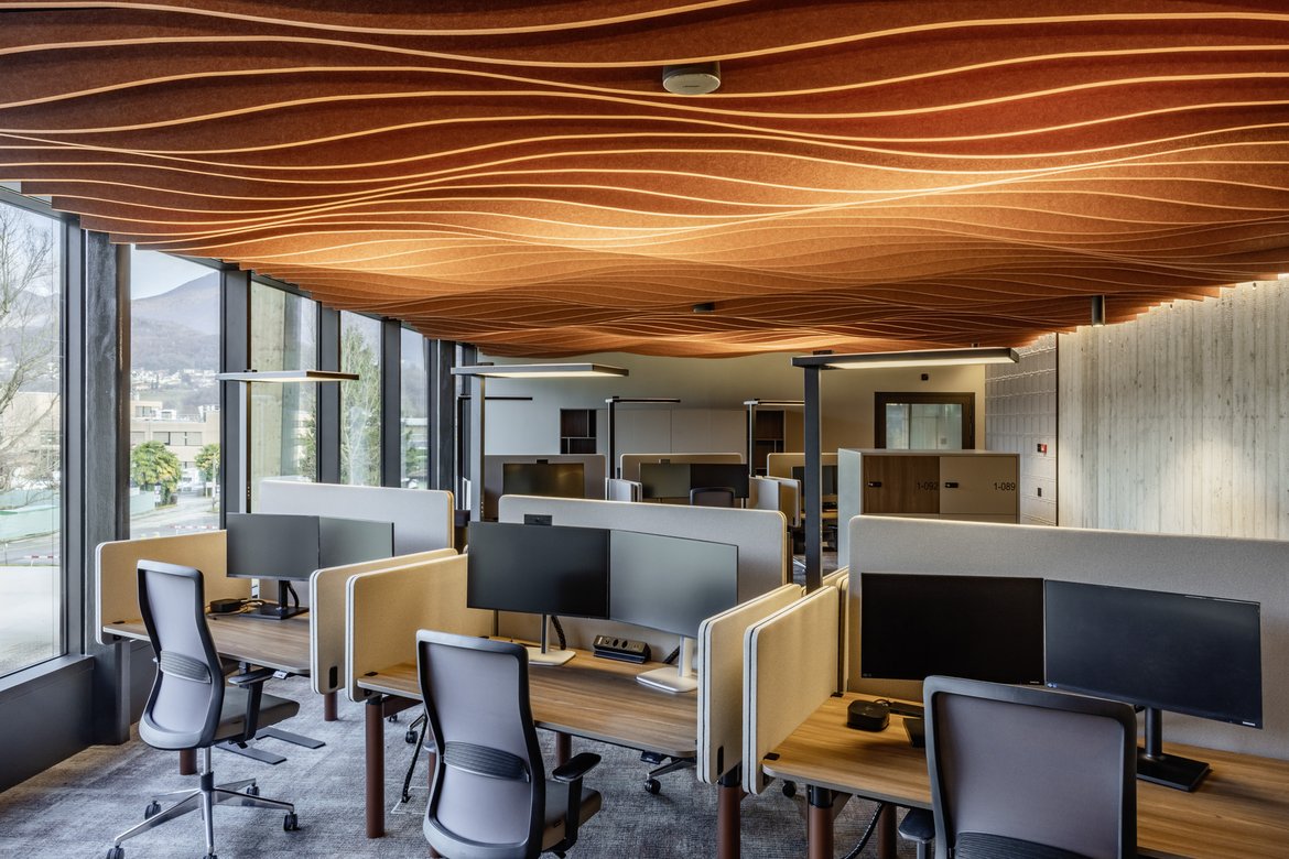 Viseca Payment Services SA - A modern office building has been constructed in Bioggio for Viseca Payment Services SA, featuring approximately 2,750 square meters of office space designed with a consistent focus on comfort, energy efficiency, and sustainability. With a sophisticated indoor climate concept combining various ceiling-mounted climate control systems, acoustic elements, and efficient energy sources, the project demonstrates how demanding usage requirements and resource-efficient operation can be combined in a modern work environment.